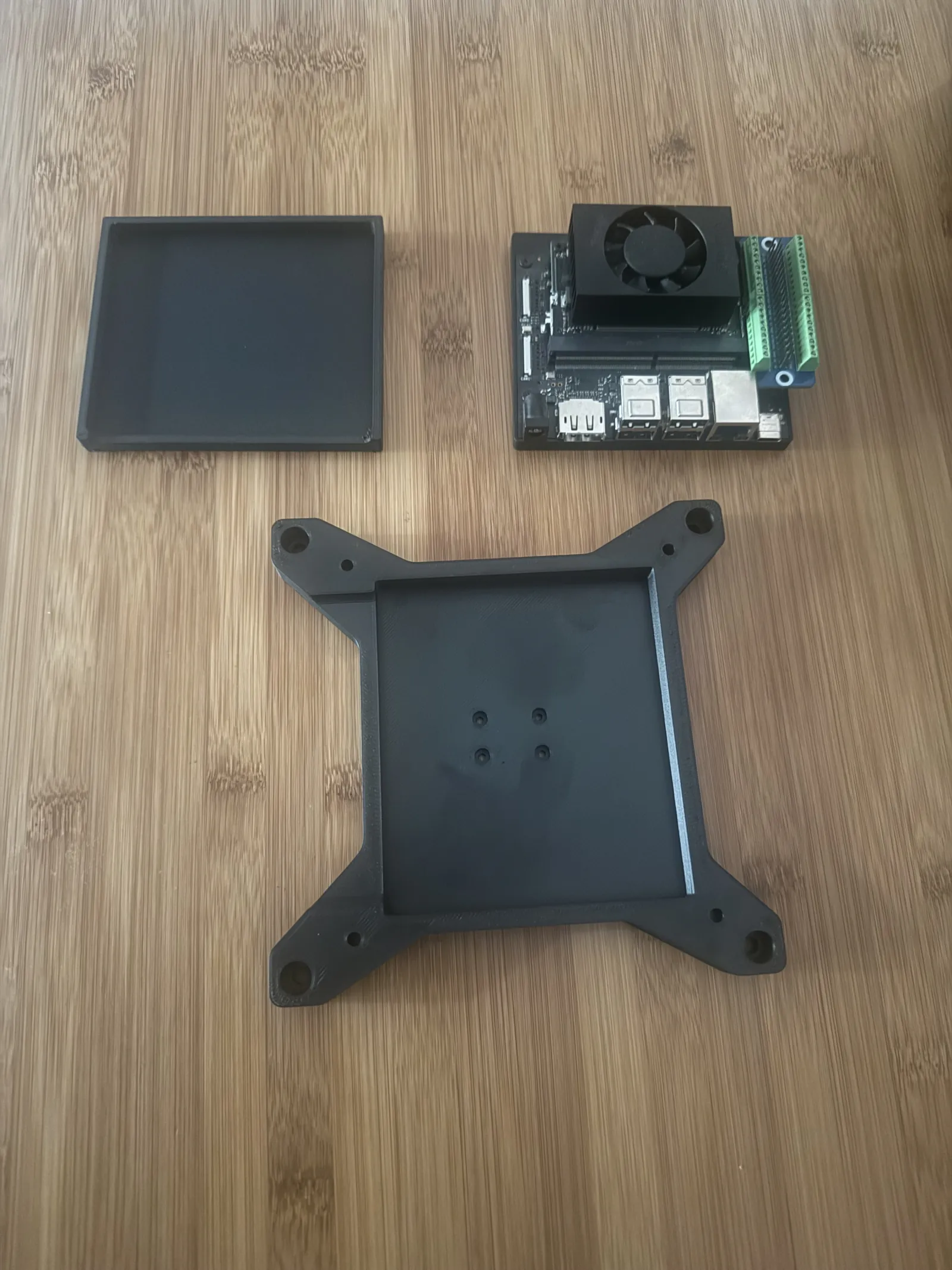 Black PET-CF and Varioshore printed parts: a shallow tray, a compute board mounted on a printed base, and a four-armed mounting bracket